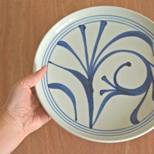 砥部焼・梅山窯　ひとつからくさの大皿(9寸)を手に持って